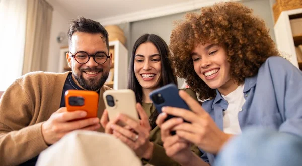 Sorrindo Diversos Amigos Relaxando no Sofá Compartilhando Risadas Enquanto Interage com Smartphones