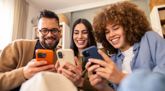 Sorrindo Diversos Amigos Relaxando no Sofá Compartilhando Risadas Enquanto Interage com Smartphones