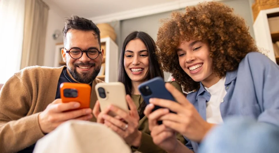 Sorrindo Diversos Amigos Relaxando no Sofá Compartilhando Risadas Enquanto Interage com Smartphones