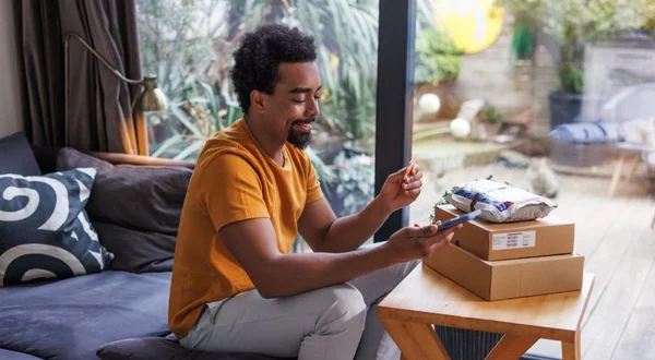 Homem sorrindo enquanto faz compras online com smartphone e um cartão de crédito em casa
