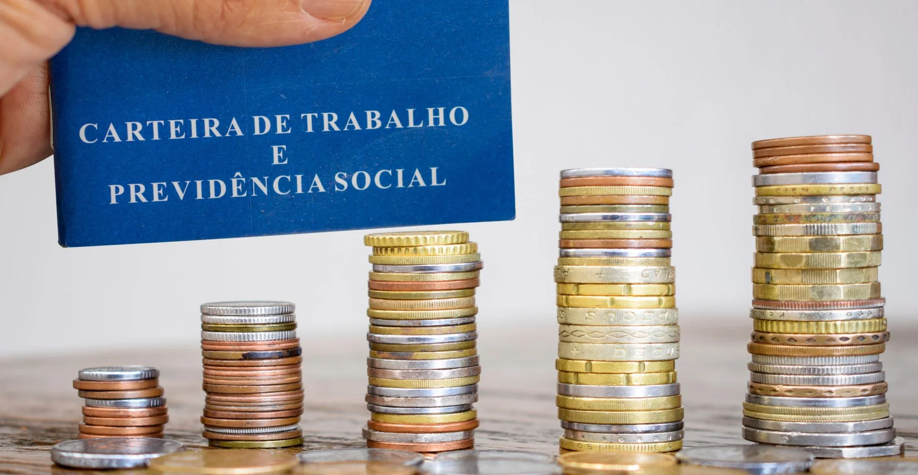 Carteira de Trabalho Brasileira com pilhas de moedas em cima da mesa. Conceito de emprego e economia. Texto em português "Cartão de Trabalho e Segurança Social".