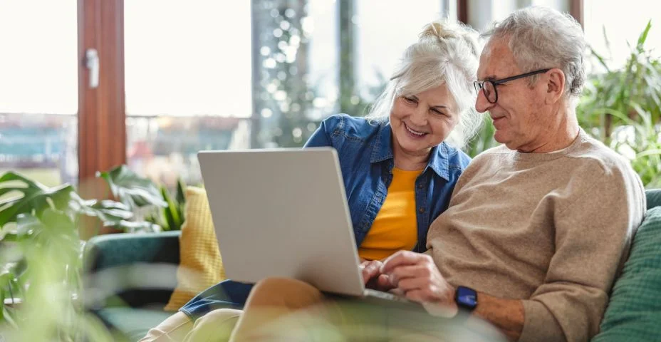 Casal de idosos usando laptop enquanto estão sentados no sofá da sala de estar em casa