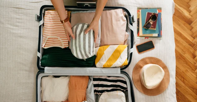 Pessoa arrumando uma mala de viagem com suas roupas e seus pertences.