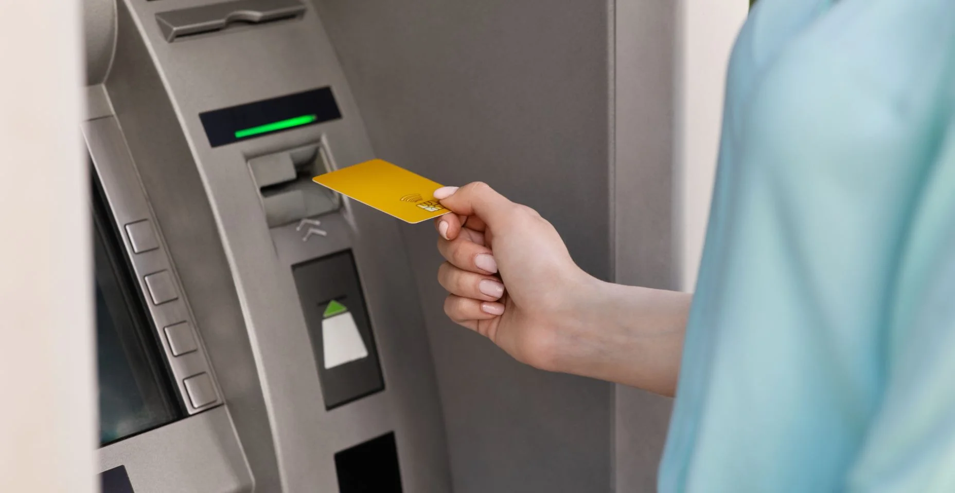 Mulher irreconhecível colocando cartão de crédito dourado em caixa eletrônico ao ar livre para pegar dinheiro
