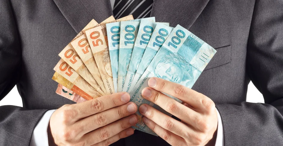 Um empresário de terno mostrando dinheiro brasileiro