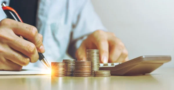 Empresário trabalhando usando calculadora com moedas de dinheiro para planos de contabilidade em pilha de mesa de madeira no escritório em casa, Vista frontal com espaço de cópia.