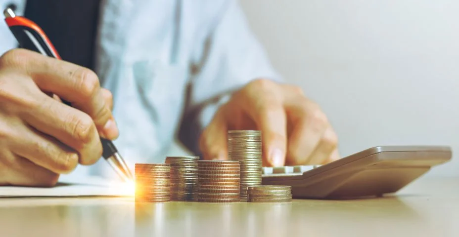 Empresário trabalhando usando calculadora com moedas de dinheiro para planos de contabilidade em pilha de mesa de madeira no escritório em casa, Vista frontal com espaço de cópia.