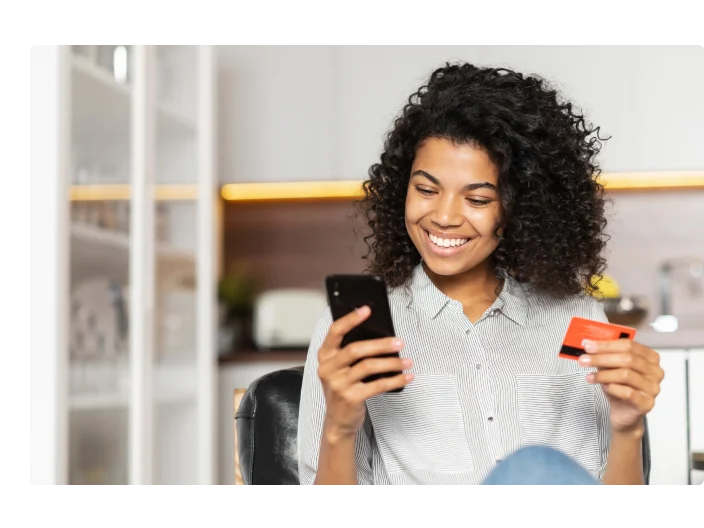 Mulher olhando seu celular com um cartão na mão para ilustrar artigo sobre cartões pré-pagos