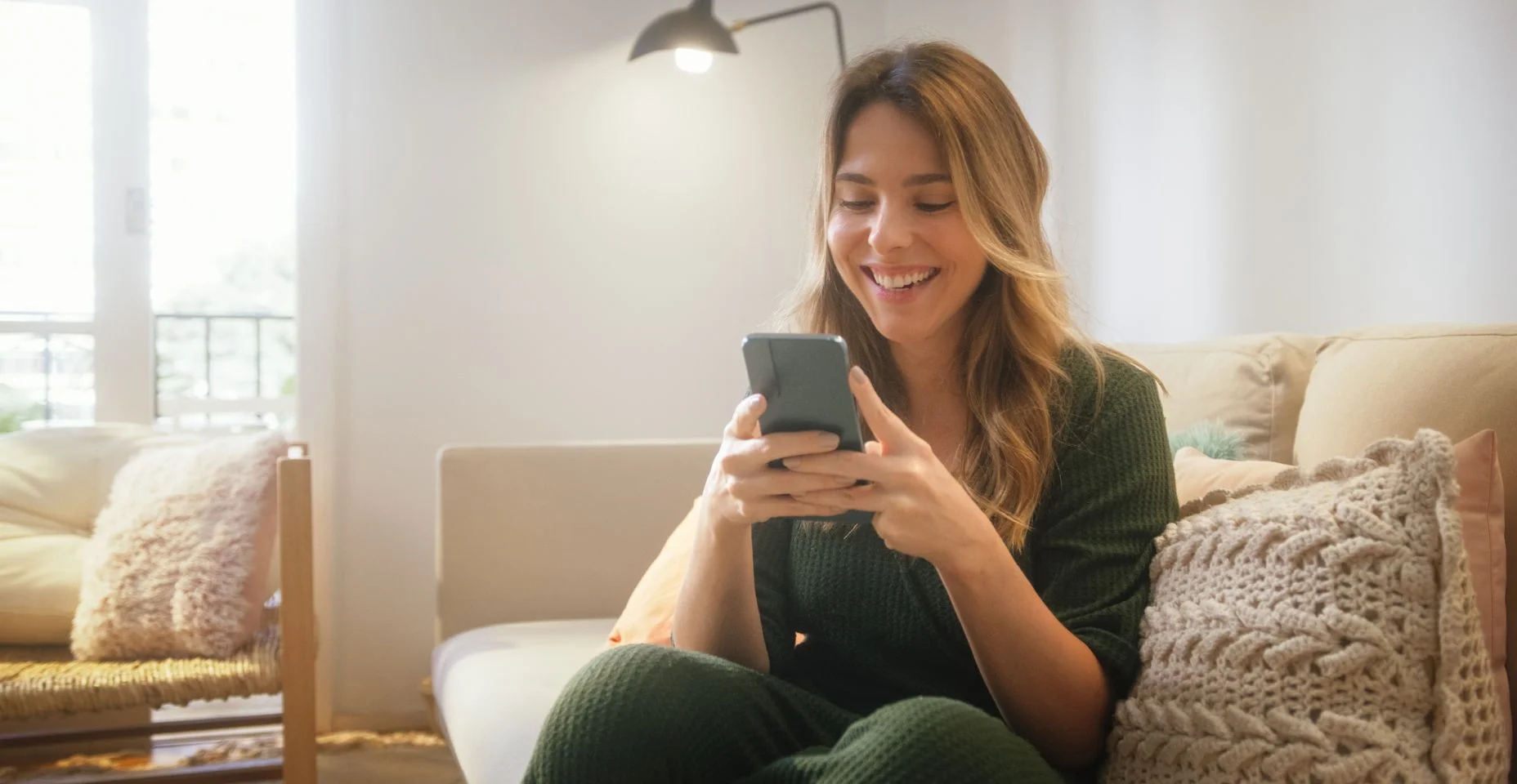 Retrato de bela mulher caucasiana usando smartphone na sala de estar elegante enquanto descansa no sofá aconchegante. Jovem em casa, fazendo compras on-line, enviando mensagens para amigos, postando nas mídias sociais