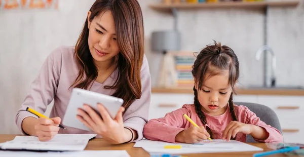 Jovem mãe verificando suas finanças enquanto sua filha está brincando ao lado dela