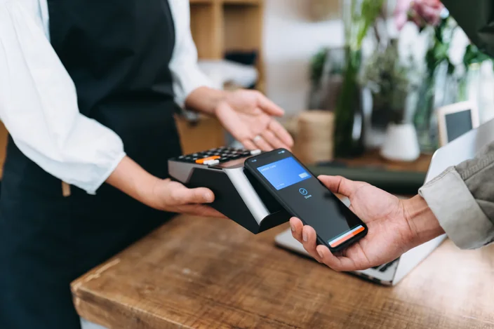 Feche acima do jovem asiático fazendo compras na floricultura. Ele está pagando com seu smartphone, digitalizar e pagar uma conta em uma máquina de cartão fazendo um pagamento rápido e fácil sem contato. Tecnologia NFC, conceito de tap and go