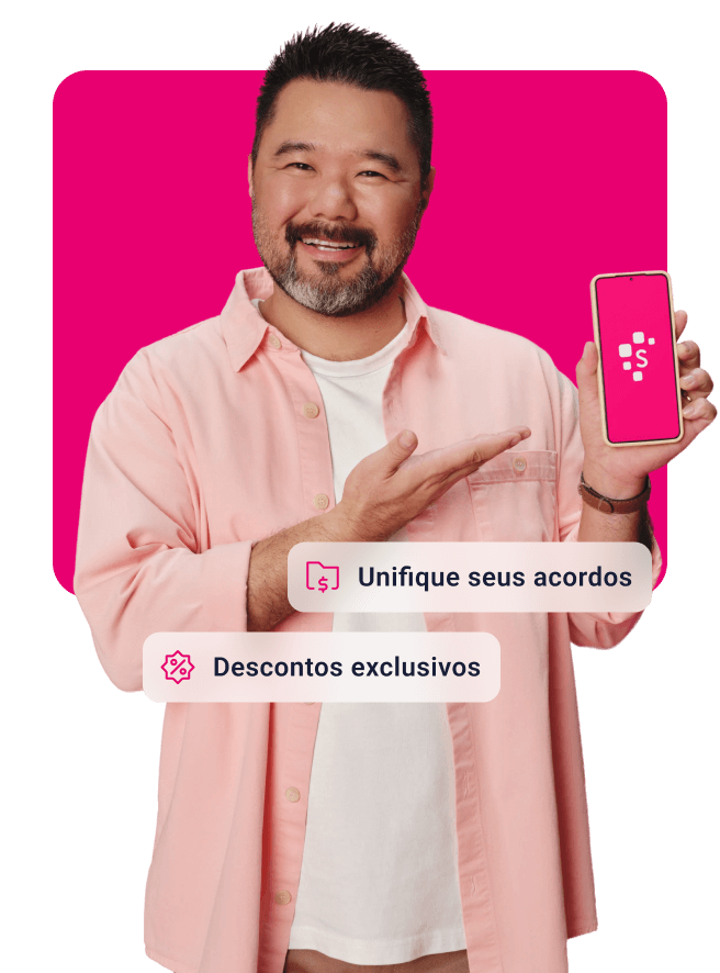 Homem de cabelos curtos e barba grisalha, sorrindo em direção à câmera enquanto segura um smartphone com tela cor-de-rosa com o logotipo da Serasa