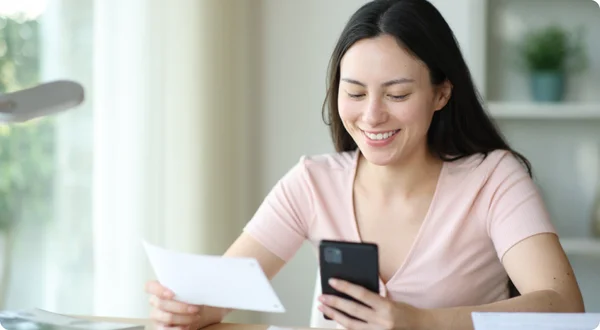 Mulher asiática feliz que guarda a conta que paga com telefone em casa