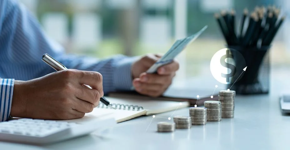 Homem segurando nota de dólar Manter um registro do valor que ele acumula ao longo do ano com esta pilha de moedas e calculadoras de cofrinho para futuros investimentos empresariais.
