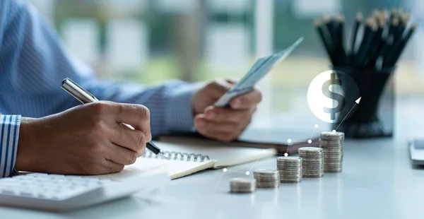 Homem segurando nota de dólar Manter um registro do valor que ele acumula ao longo do ano com esta pilha de moedas e calculadoras de cofrinho para futuros investimentos empresariais.