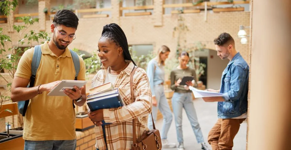 Estudantes, faculdade e aprendizagem, tablet e livros para educação, bolsa de estudos e colaboração no corredor do campus. Universidade com pessoas estudando juntas, aprenda com diversidade e objetivos acadêmicos