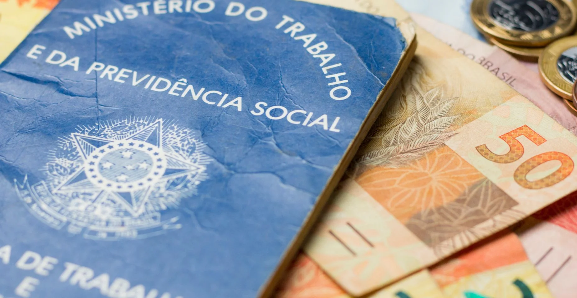 Notas de dinheiro acompanhado de moedas, carteira de trabalho, lupa, calculadora encima da mesa