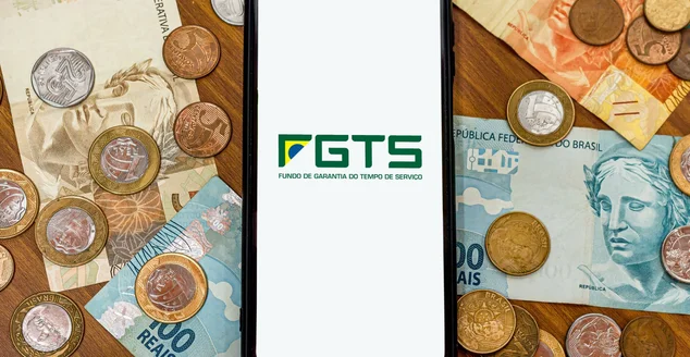 Logotipo do FGTS na tela do smartphone com diversas moedas e dinheiro ao redor. O FGTS é o fundo de garantia do trabalhador brasileiro. Pagamento pelo governo brasileiro