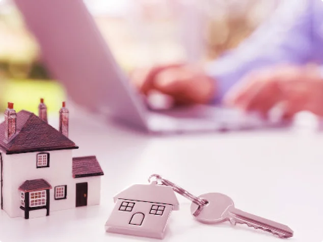 casa pequena, chave e alguem mexendo em um computador no fundo