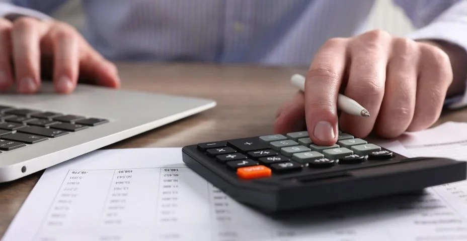 Homem usando calculadora enquanto trabalha no laptop na mesa, closeup