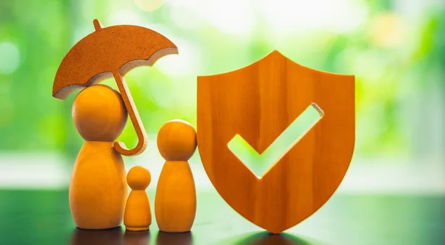 Uma escultura de madeira de uma família está junto sob um guarda-chuva com um símbolo de seguro. Isso representa o conceito de cobertura de seguro familiar e de grupo