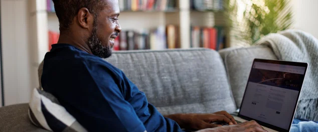 Homem sorridente relaxado sentado no sofá e usando laptop