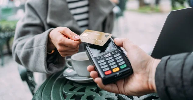 Jovem pagando sem contato com cartão de crédito em um café na calçada.