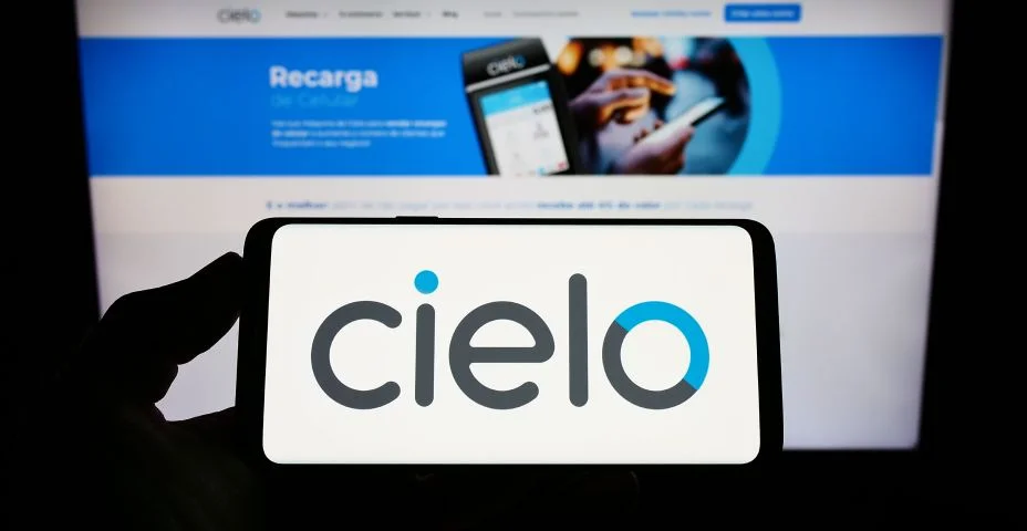 Pessoa segurando smartphone com logotipo da empresa brasileira de pagamentos Cielo S.A. na tela na frente do site. Concentre-se na tela do telefone.