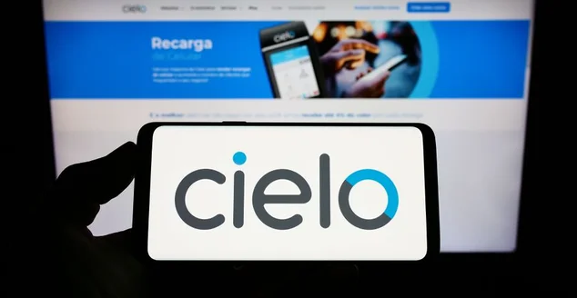 Pessoa segurando smartphone com logotipo da empresa brasileira de pagamentos Cielo S.A. na tela na frente do site. Concentre-se na tela do telefone.