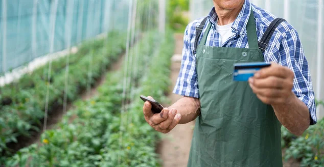 Agricultor sênior usando cartão de crédito em estufa