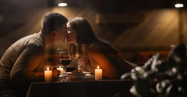 Casal apaixonado comemorando o Dia dos Namorados jantando em casa, se beijando, vista pela janela