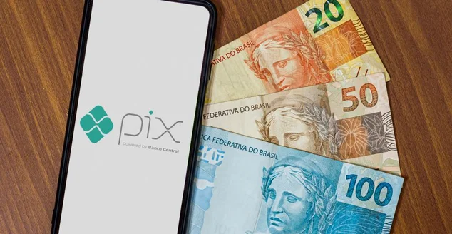 Logotipo Pix na tela do smartphone com diversas moedas ao redor. Pix é o novo sistema de pagamentos e transferências do governo brasileiro e brasileiro.