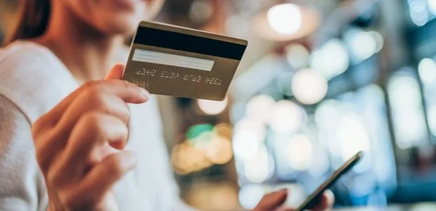 Recorte de uma mulher segurando um cartão de crédito enquanto digita no seu celular
