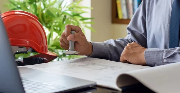 Arquiteto ou engenheiro homem carimbando carimbador de borracha na papelada do projeto no escritório.
