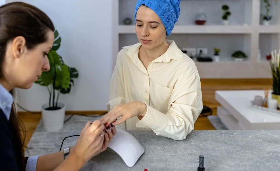 Uma maquiadora profissional está polindo as unhas de uma mulher em uma sala de estar.