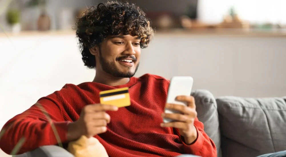 omem sorridente usando smartphone e cartão de crédito em casa