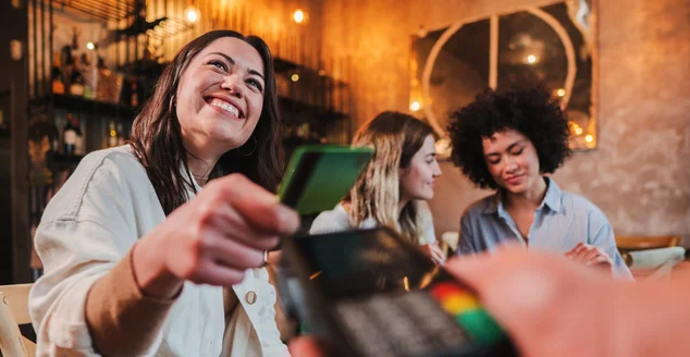 Mulher jovem feliz pagando conta com um cartão de crédito sem contato em um restaurante. Mulher sorrindo segurando um cartão de crédito e dando uma transação de pagamento ao caixa.