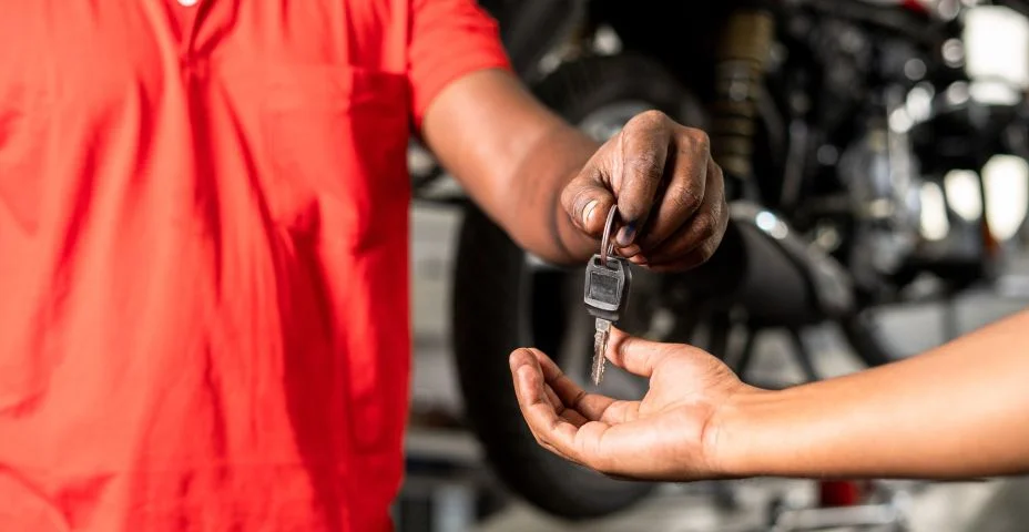 Close-up das mãos mecânicas de motocicleta dando chave de motobike ao cliente após serviço de manutenção na garagem - conceito de serviço de reparo de conclusão bem-sucedido