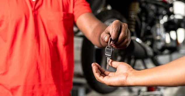 Close-up das mãos mecânicas de motocicleta dando chave de motobike ao cliente após serviço de manutenção na garagem - conceito de serviço de reparo de conclusão bem-sucedido