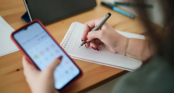 Jovem mulher usando telefone celular para calcular seu orçamento doméstico