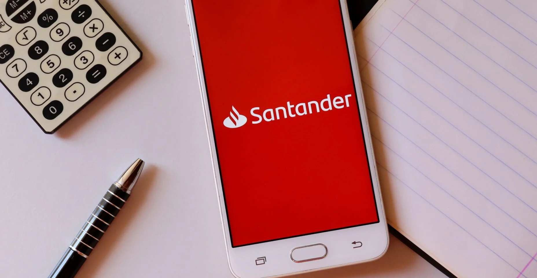Aplicativo do banco Santander na tela do smartphone na mesa de escritório com calculadora e caneta. Conceito de internet banking do Santander.