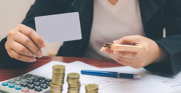 Mulher de negócios segurando simular cartão de crédito ou cartão de visita em branco e usando smartphone na mesa de trabalho com pilha de moedas e trabalho de papel em casa ou escritório para negócios de comércio eletrônico ou compras on-line sem d