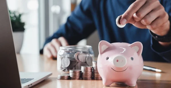 Mão colocando moedas em um cofrinho para economizar dinheiro e salvar dinheiro conceito
