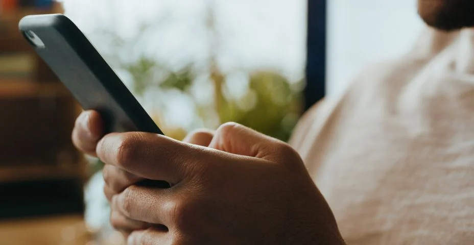 Tiro cortado de um empresário irreconhecível sentado sozinho e usando seu celular em seu escritório de origem