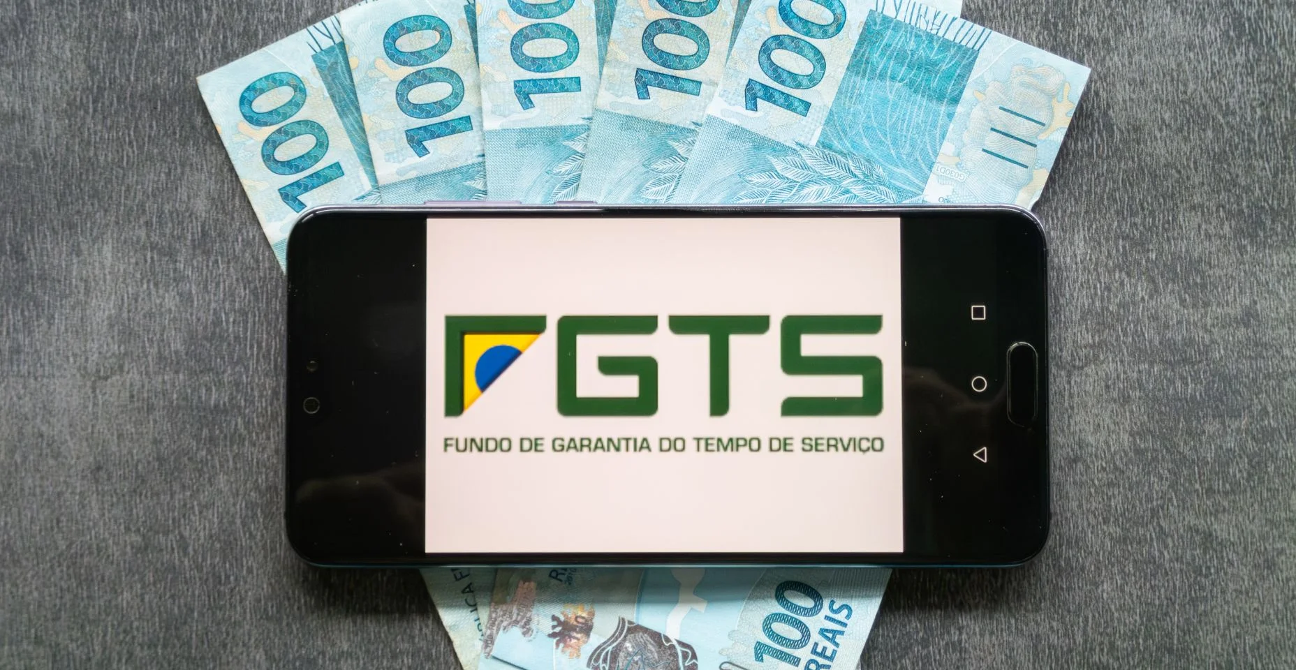 Aplicação do FGTS (Fundo Garantidor do Brasil) na tela do smartphone sobre cédulas de cem reais