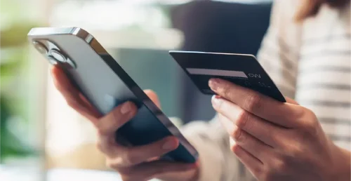 Mulher segurando cartões de crédito e usando smartphone para fazer compras online com pagamento no internet banking.