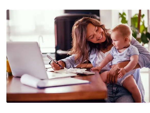 mãe com beber no colo sorrindo e de frente para o notebook