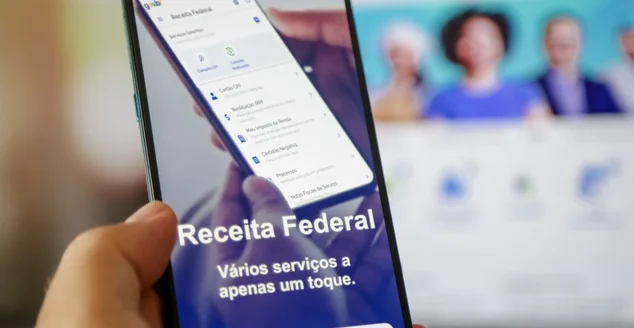 Imposto de renda 2024 da receita federal segurando celular com aplicativo e dinheiro