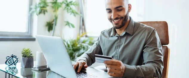 Meio adulto sorridente empresário latino no escritório, usando cartão de crédito para pagar online