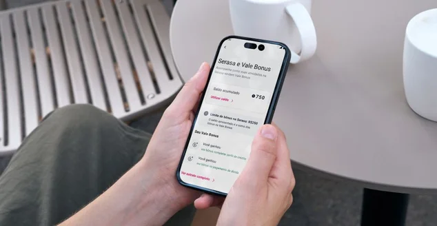 Uma pessoa segura um smartphone com a tela exibindo um aplicativo de serviços financeiros em português, relacionado ao "Serasa e Vale Bonus". A interface mostra um "Saldo acumulado: 750", um "Limite de bônus no Serasa: R$1250" com renovação semestral, e uma seção chamada "Seus Vales Bonus" com três itens "Você pontua". Há também um botão "Ver extrato completo >".